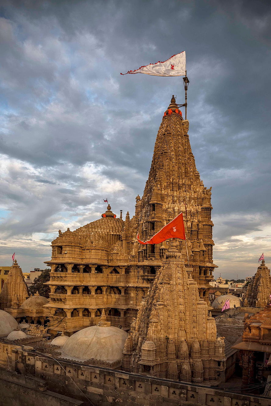Dwarkadhish Temple in Dwarka India with ornate stone shikhara and fluttering flags under a dramatic cloudy sky HD phone wallpaper