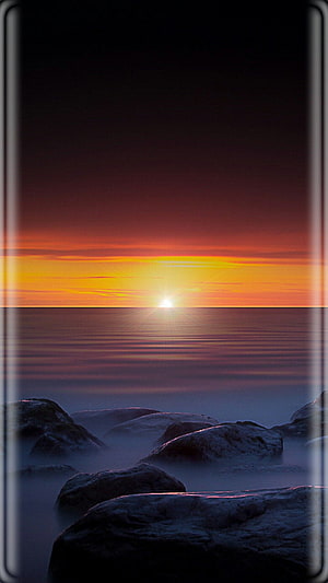 Serene Ocean Sunset Over Misty Rocks With Vibrant Orange Sky HD phone wallpaper
