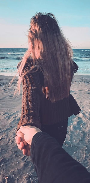 Couple holding hands on a sandy beach with ocean waves in the background HD phone wallpaper