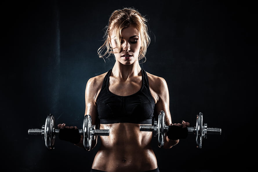 Athletic Woman Performing Bicep Curls With Dumbbells In Dark Studio Setting HD wallpaper