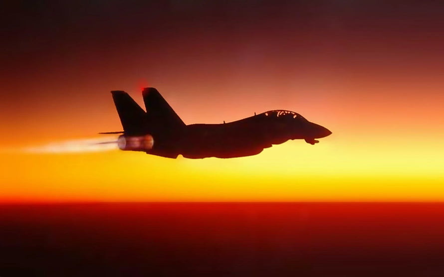 F-14 Tomcat fighter jet silhouette with afterburner against a fiery orange sunset sky HD wallpaper