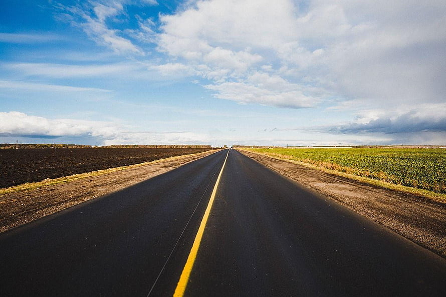 Endless Highway Stretching Through Open Farmland Under a Bright Blue Sky HD wallpaper