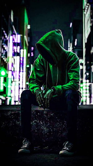 Lone figure in green hoodie sitting on a ledge against a neon-lit urban night backdrop HD phone wallpaper