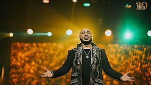 B Praak performing on stage with arms open under warm concert lighting HD wallpaper