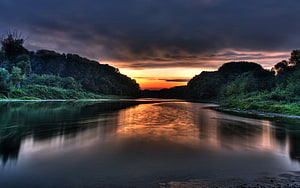 Dramatic River Sunset with Dark Clouds and Golden Reflections on Calm Water HD wallpaper