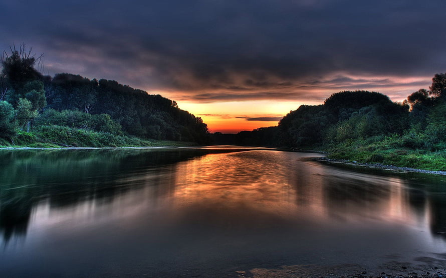 Dramatic River Sunset with Dark Clouds and Golden Reflections on Calm Water HD wallpaper