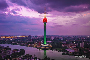 Lotus Tower illuminated in green and red against a dramatic purple twilight sky over a cityscape and lake HD wallpaper
