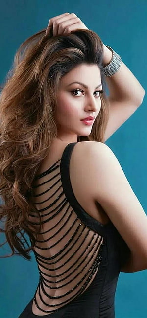 Urvashi Rautela in a black strappy back dress with long wavy hair against a teal studio background HD phone wallpaper