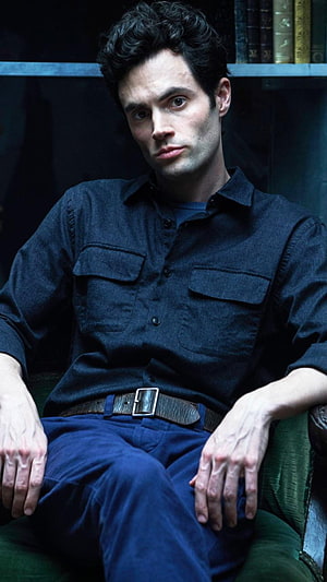 Joe Goldberg from You in a dark blue shirt seated in a moody library setting HD phone wallpaper