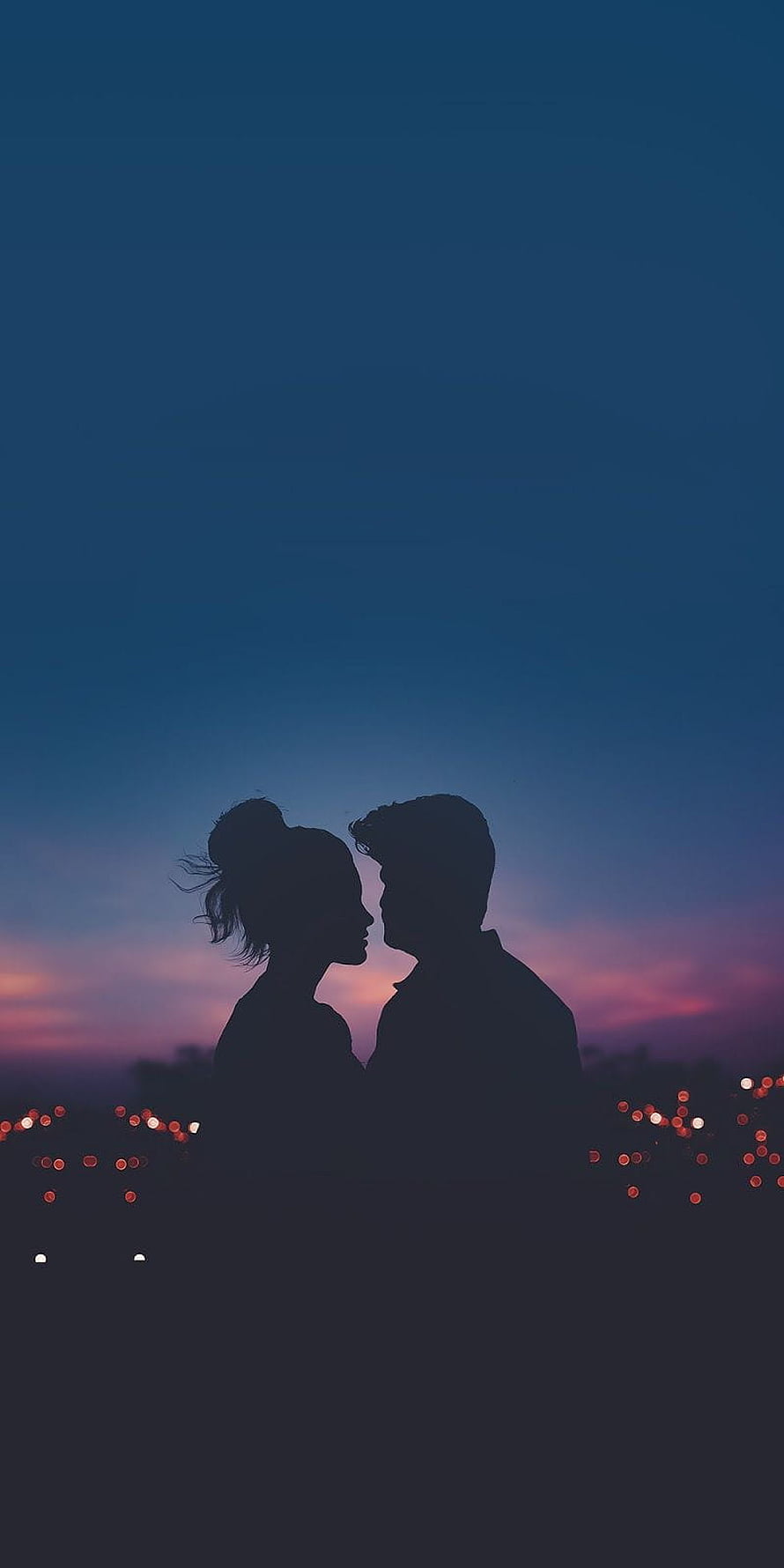 Silhouette of a romantic couple facing each other against a twilight sky with city bokeh lights HD phone wallpaper