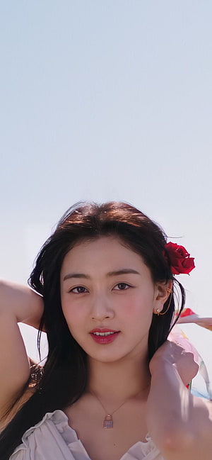 Jihyo from TWICE in a soft white top with a red rose tucked in her hair against a bright sky HD phone wallpaper
