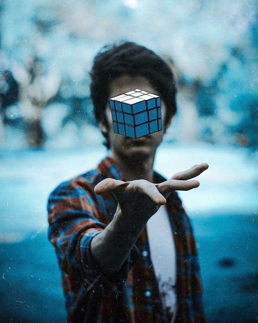 Young man holding a floating Rubik's cube over his face in a moody blue-toned outdoor scene HD phone wallpaper
