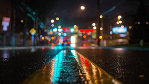 Rain-soaked city street at night with glowing bokeh lights reflecting on wet asphalt HD wallpaper