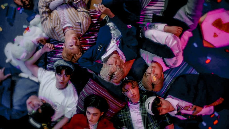 Stray Kids members lying on colorful striped bedding with plush toys and vibrant pink lighting HD wallpaper