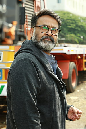 Mohanlal in a dark coat and glasses standing before a red truck HD phone wallpaper