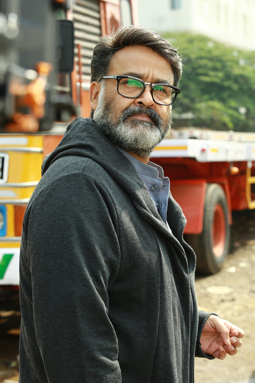 Mohanlal in a dark coat and glasses standing before a red truck HD phone wallpaper