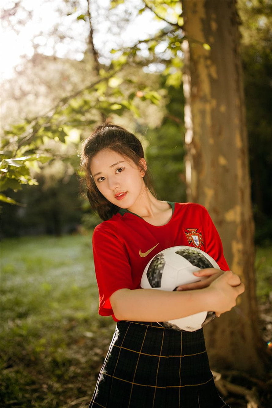 Zhao Lusi in a red Portugal football jersey holding a soccer ball in a sunlit park HD phone wallpaper