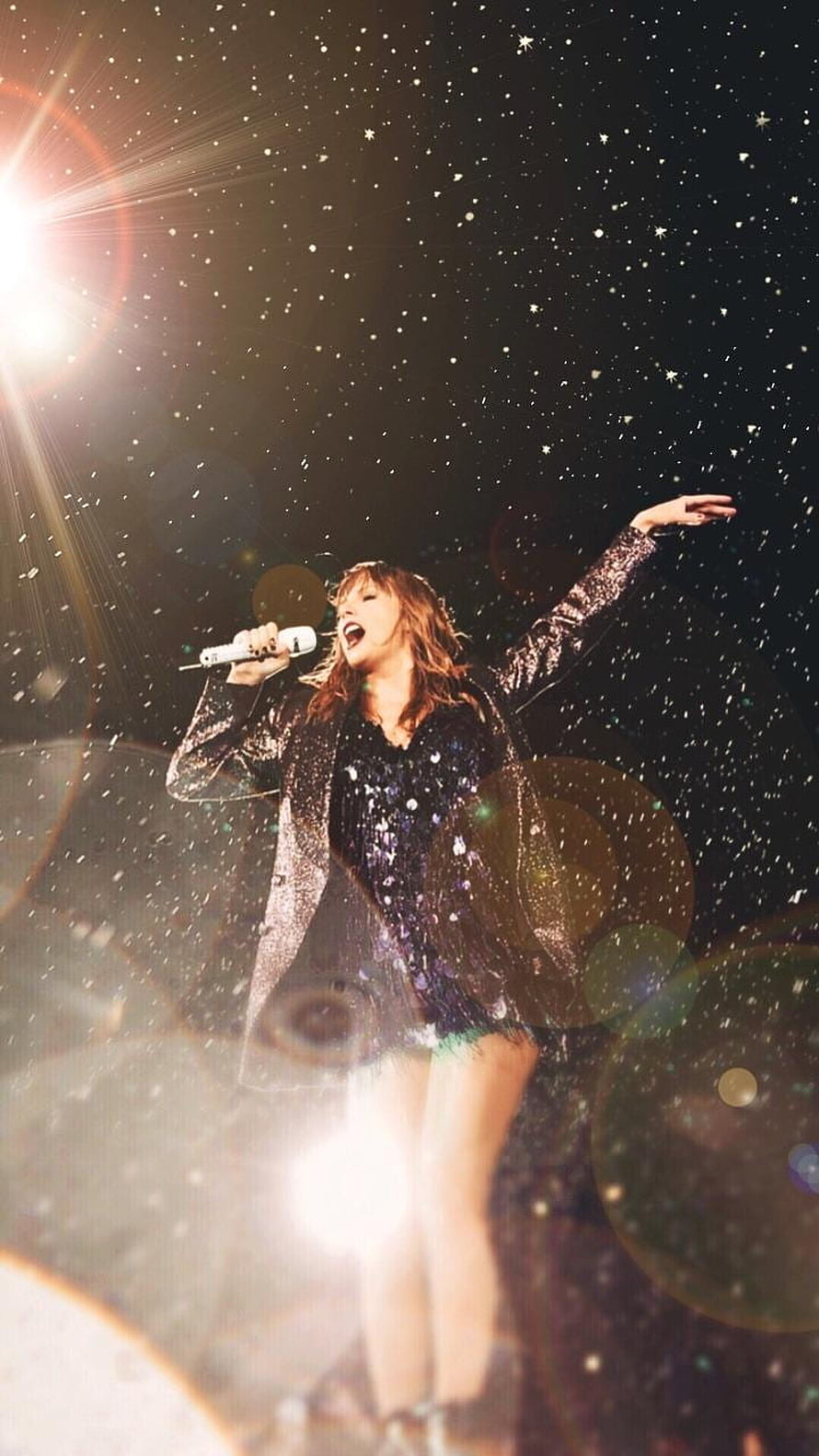 Taylor Swift performing on stage in a sparkling sequined outfit with dramatic concert lighting and falling confetti HD phone wallpaper