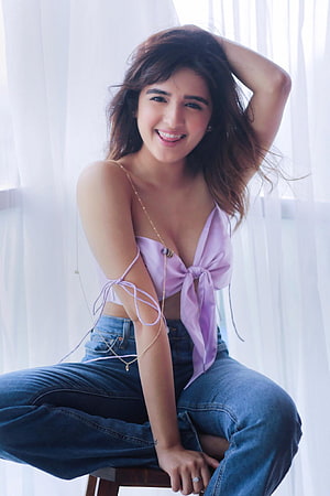 Shirley Setia in a lavender top and denim jeans sitting by a bright window HD phone wallpaper