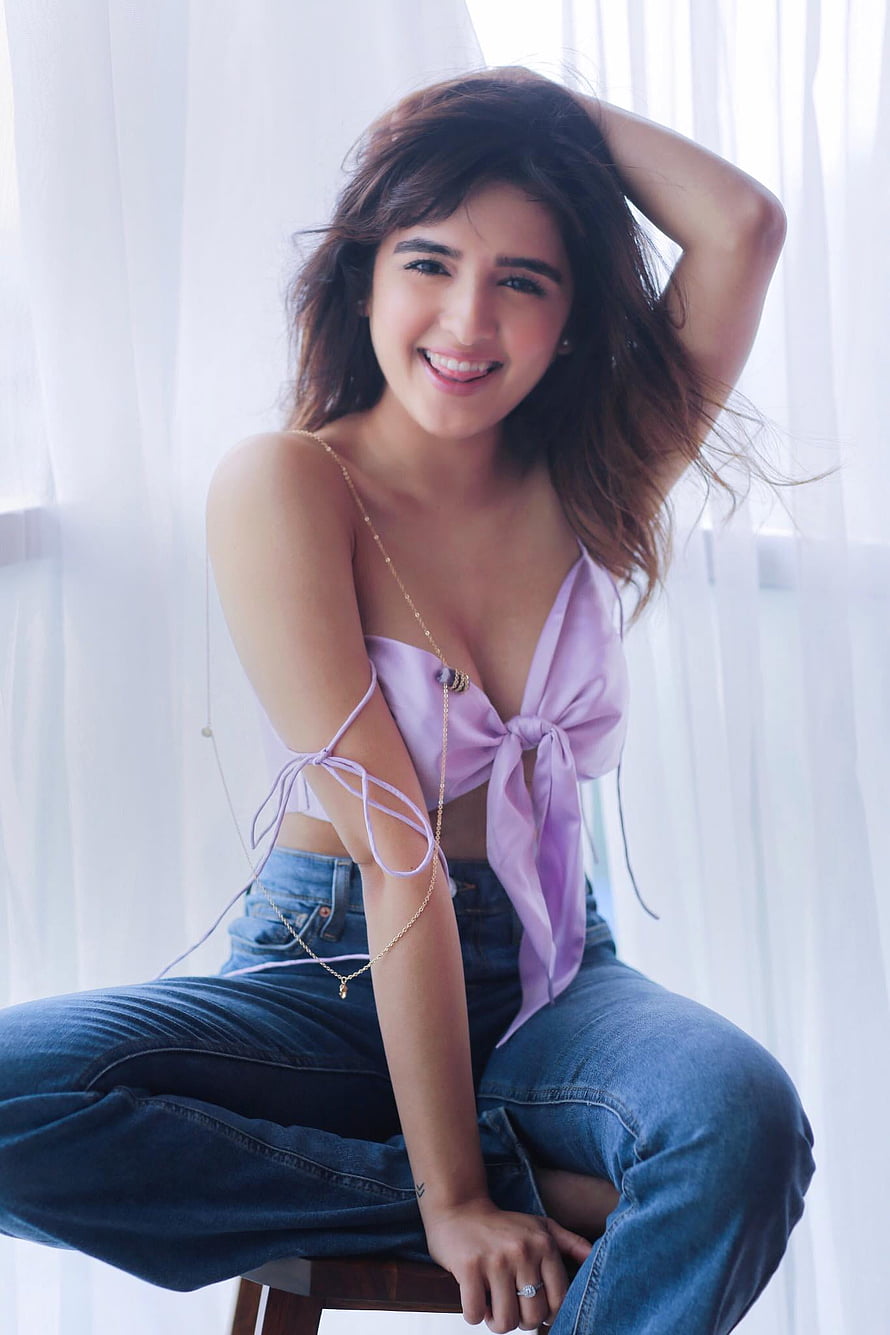 Shirley Setia in a lavender top and denim jeans sitting by a bright window HD phone wallpaper
