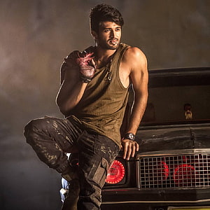 Vijay Devarakonda in gritty action pose on a vintage car with red grille lights HD phone wallpaper