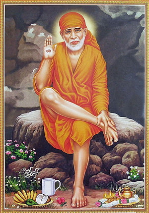 Sai Baba Portrait in Orange Robes Seated on Rock with Offerings and Flowers HD phone wallpaper
