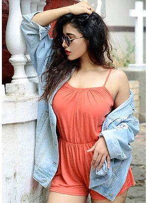 Ketika Sharma in a coral romper and distressed denim jacket leaning against a white balustrade HD phone wallpaper