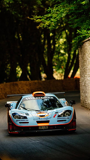 McLaren F1 GTR race car navigating a tree-lined road with Warsteiner livery HD phone wallpaper
