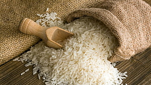 Uncooked white rice spilling from a burlap sack with a wooden scoop on a rustic wooden surface HD wallpaper
