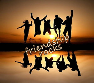 Silhouetted friends jumping at sunset with friendship rocks text and water reflection HD wallpaper