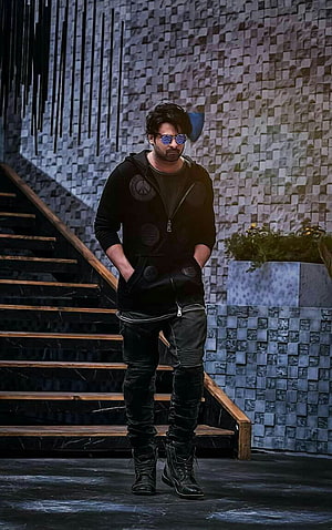Prabhas in all-black streetwear with sunglasses standing before a textured stone wall and staircase HD phone wallpaper