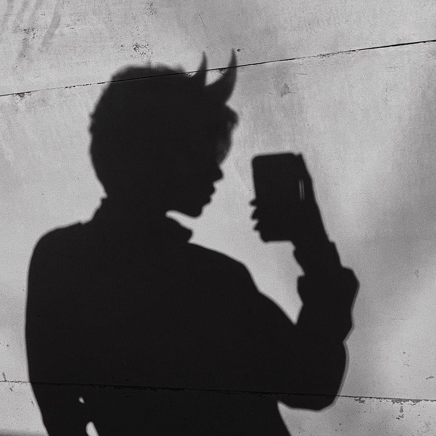 Silhouette of a horned figure holding a smartphone against a textured concrete wall HD wallpaper