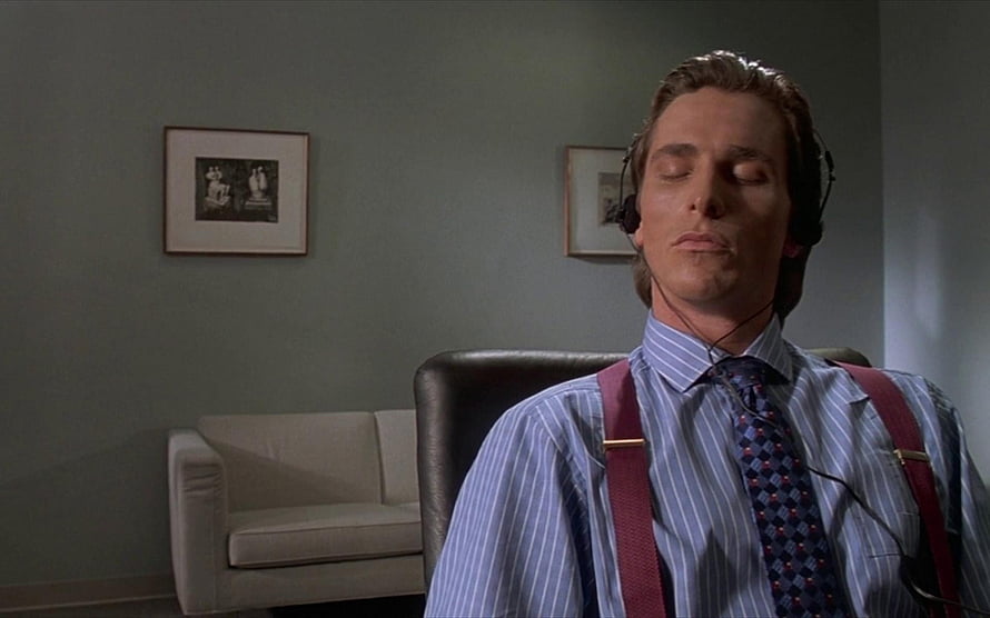 Patrick Bateman in a striped shirt and suspenders with headphones in a minimalist office HD wallpaper