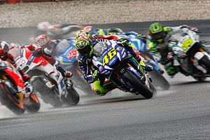 MotoGP Riders Cornering Through Wet Track Spray in High-Speed Racing Action HD wallpaper