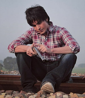 Man in plaid shirt crouching on railroad tracks holding a metal pipe HD phone wallpaper