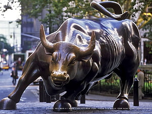Charging Bronze Bull Statue on a City Street with Urban Background HD wallpaper