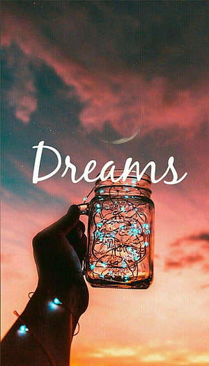 Hand Holding Glowing Fairy Light Jar Against Sunset Sky with Dreams Text HD phone wallpaper