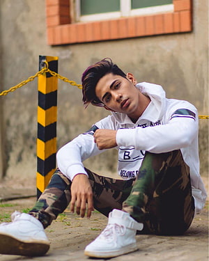 Young man in white hoodie and camouflage pants sitting on pavement HD phone wallpaper
