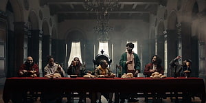 Kendrick Lamar and guests seated at a long table in a grand hall with chandeliers and arched windows HD wallpaper