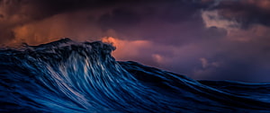 Dramatic Ocean Wave Curling Under a Stormy Sunset Sky HD wallpaper