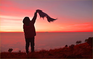 Silhouette of a person waving a scarf on a hilltop above a sea of clouds at sunset HD wallpaper