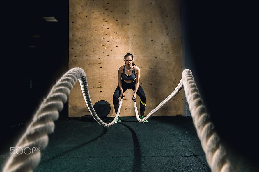 Athletic Woman Performing Battle Rope Workout in Dark Gym Setting HD wallpaper