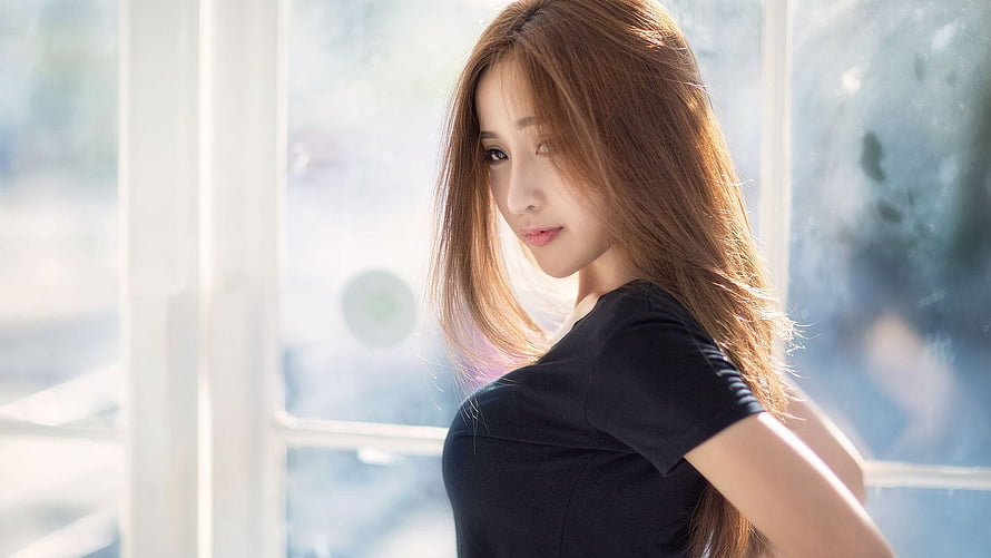Young Asian Woman in Black Top Standing by a Bright Window HD wallpaper