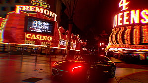 Neon-lit Fremont Casino and 4 Queens at night with a sleek black sports car HD wallpaper