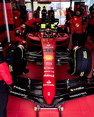 Ferrari F1 car in the pit garage with mechanics and sponsor logos HD phone wallpaper