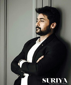 Suriya in a black suit with arms crossed leaning against a wall HD phone wallpaper