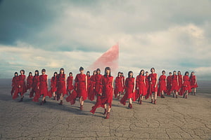 Sakurazaka46 members in red dresses walking across a cracked desert landscape under a dramatic sky HD wallpaper