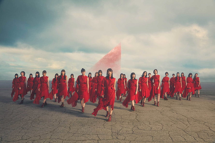 Sakurazaka46 members in red dresses walking across a cracked desert landscape under a dramatic sky HD wallpaper