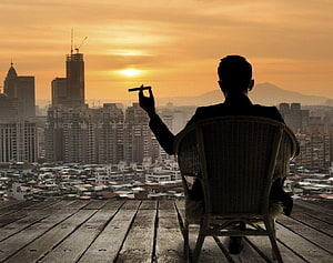 Silhouette of a man in a suit holding a cigar on a rooftop overlooking a city skyline at sunset, Billionaire Luxury Lifestyle posted by Ryan Walker, billionaire lifestyle HD wallpaper