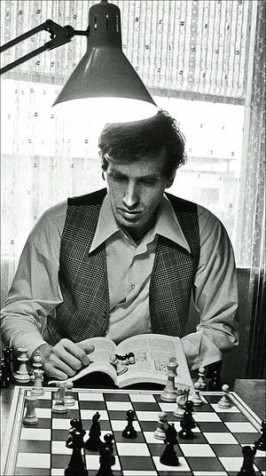 Bobby Fischer studying chess openings with a book and board in a vintage black and white photograph HD phone wallpaper